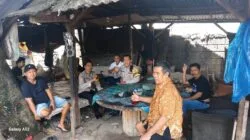 Sekelompok polisi dan warga duduk di dalam pondok sederhana, beberapa memegang makanan dan minuman.