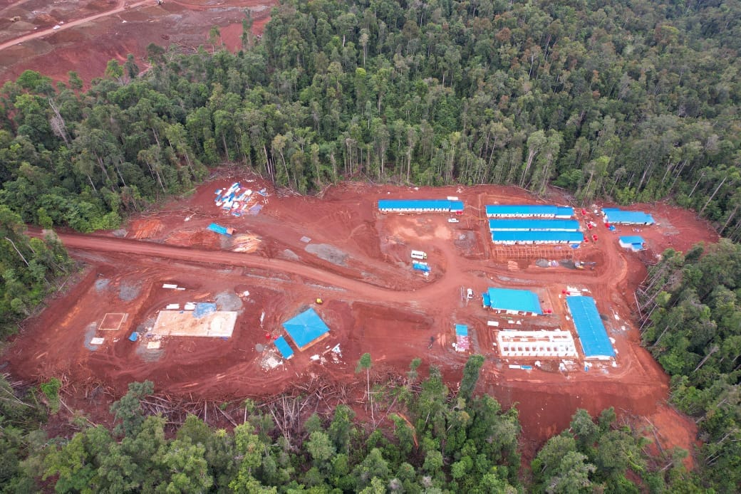 Area proyek konstruksi dengan bangunan dan jalan setapak di tengah hutan lebat.
